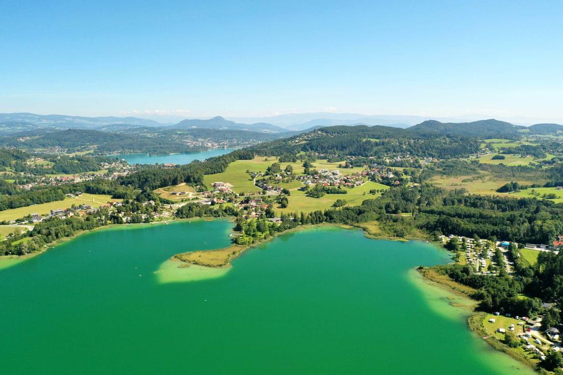 Luftaufnahme eines grünen Sees mit umliegenden Wäldern, Dörfern und Campingplatz im Sommer